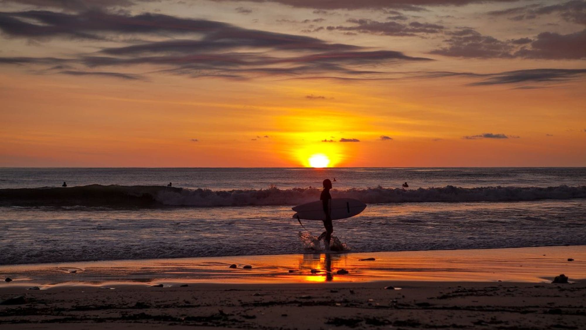Surfer silhouette walking the Santa Teresa beach at sunset