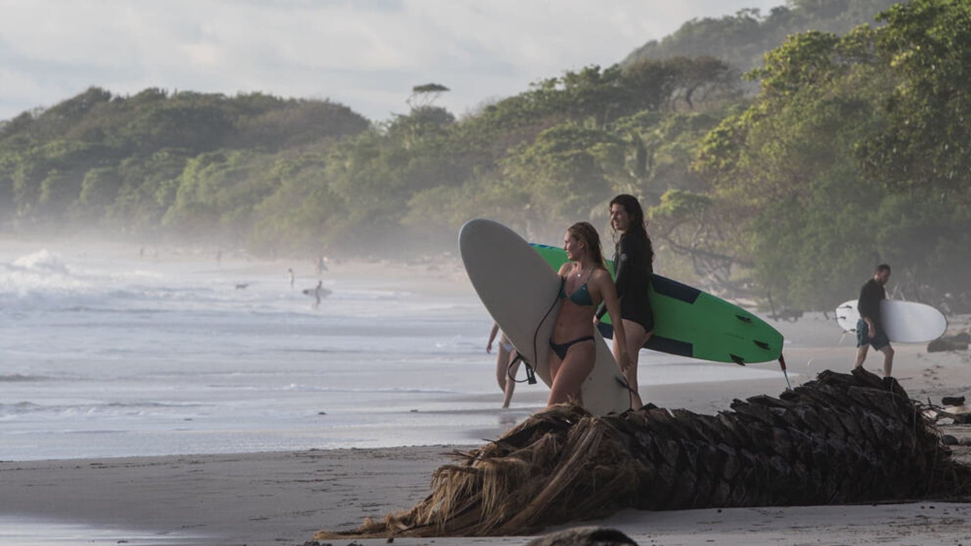 Two surfers walking down the beach with boards in the morning mist